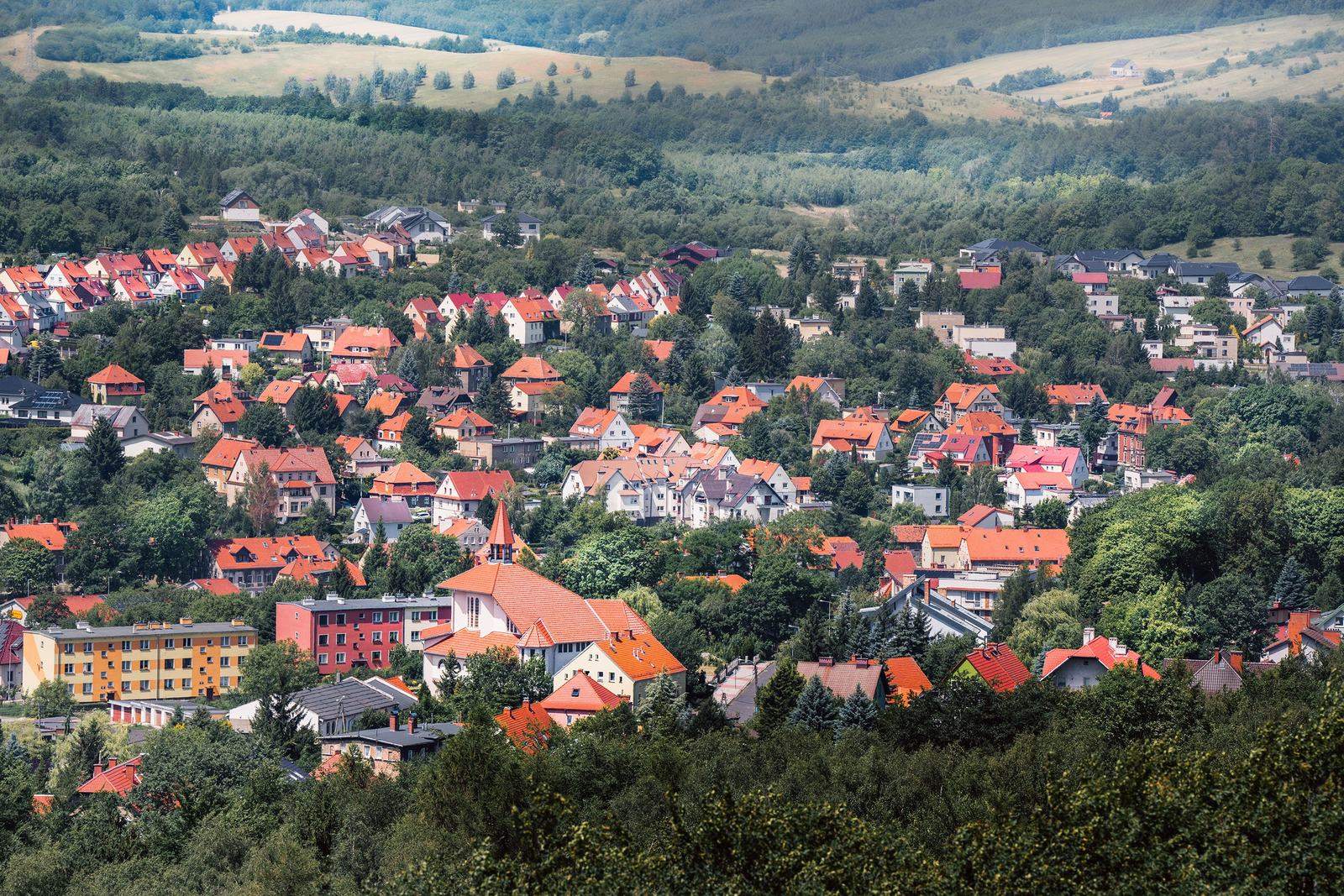 Widok z góry na małe miasto z gęstą zabudową jednorodzinną o czerwonych dachach, otoczone lasem